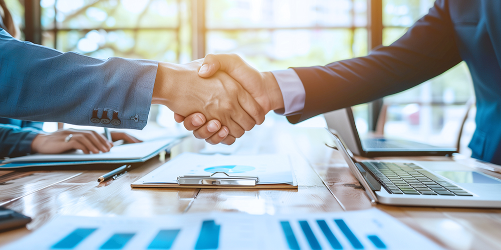 Business -Fachleute schütteln an einem Meeting -Tisch, umgeben von Laptops und Dokumenten und symbolisieren erfolgreiche Partnerschaften in der Elektrowerkzeugbranche.
